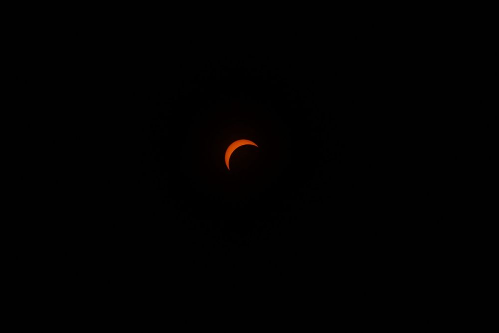 Thin orange crescent of the sun during a solar eclipse against a dark sky