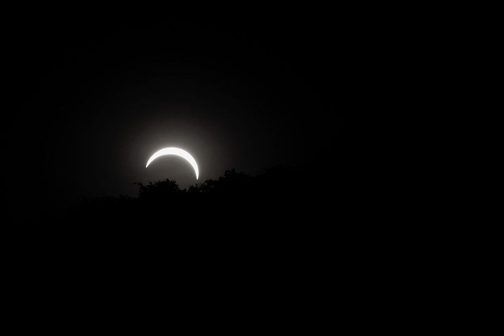 Bright crescent sun of a partial solar eclipse over a dark horizon
