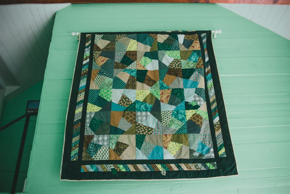 Patchwork quilt with a green and blue geometric design hanging on a mint wall