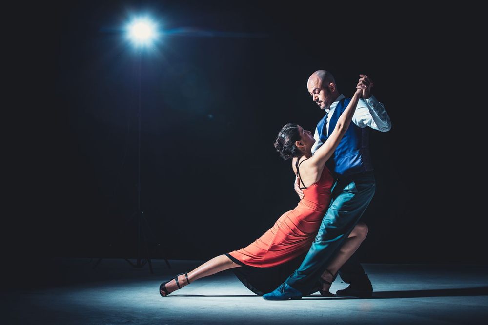 Couple dancing a tango under a spotlight on a dark stage
