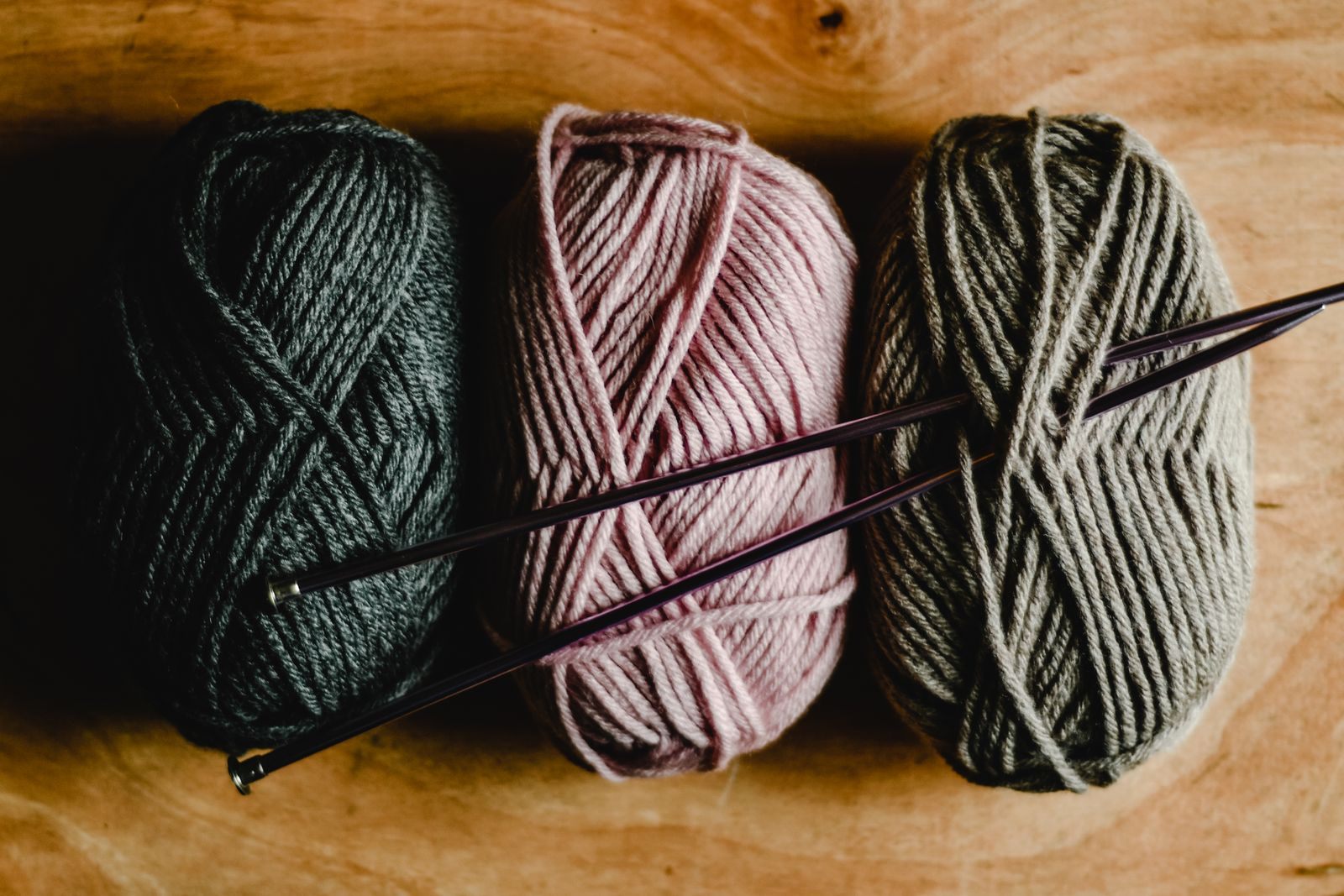 Three balls of wool with knitting needles on a wooden table, ready for knitting cruises 2027