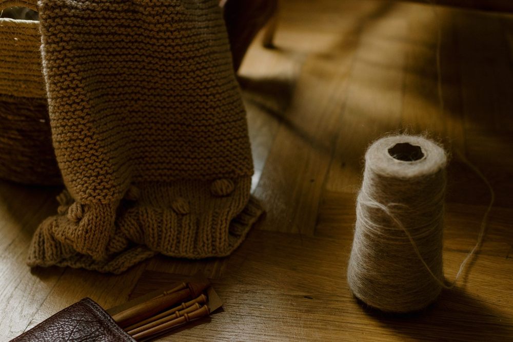 Hand-knitted wool beside a spool of twine on a wooden floor