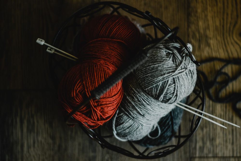 Red and gray yarn with knitting needles in a wire basket