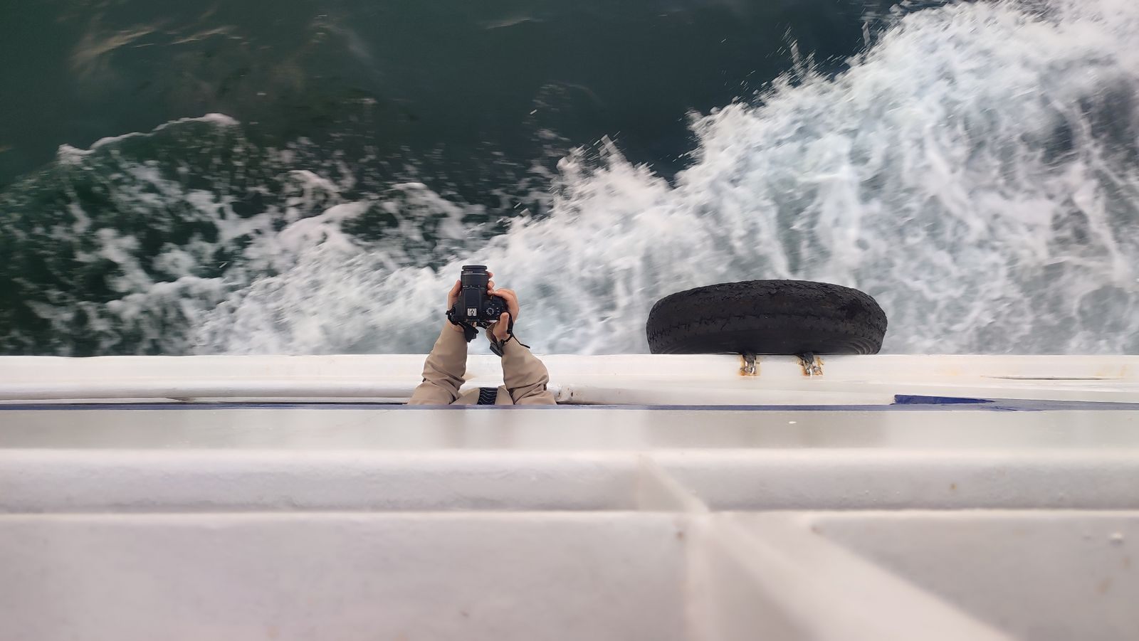 Photographer on a ship&rsquo;s deck aiming a camera at the wake and waves below