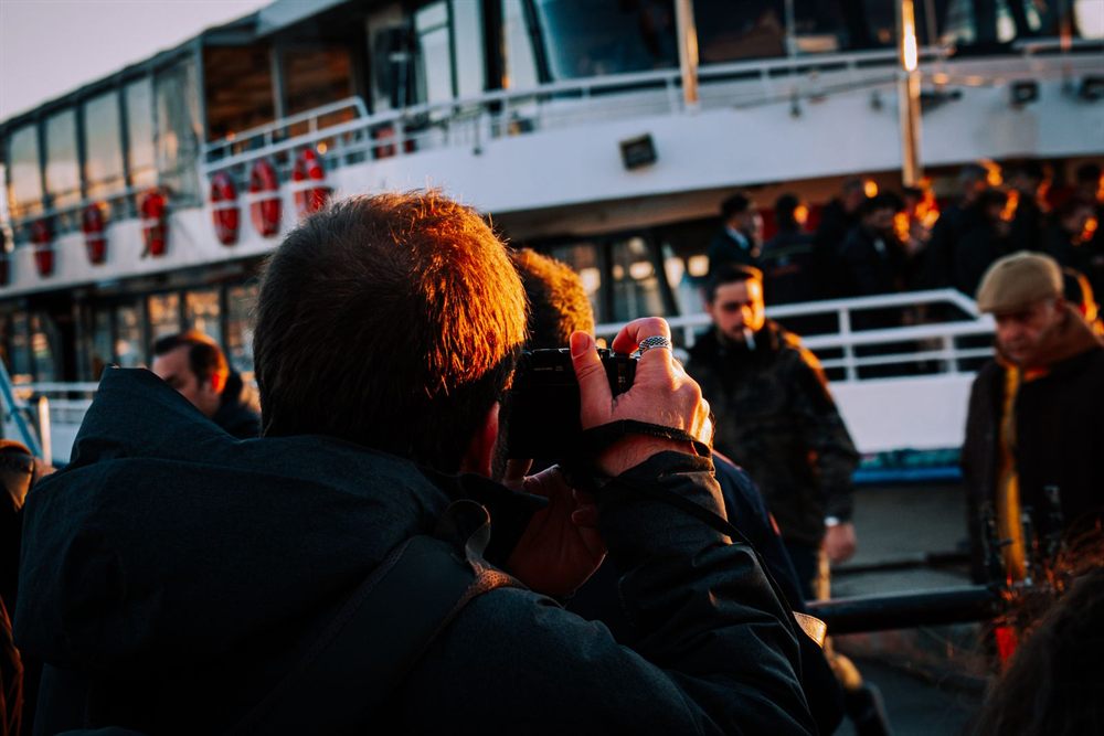 Passengers photographing the view from a crowded boat at sunset