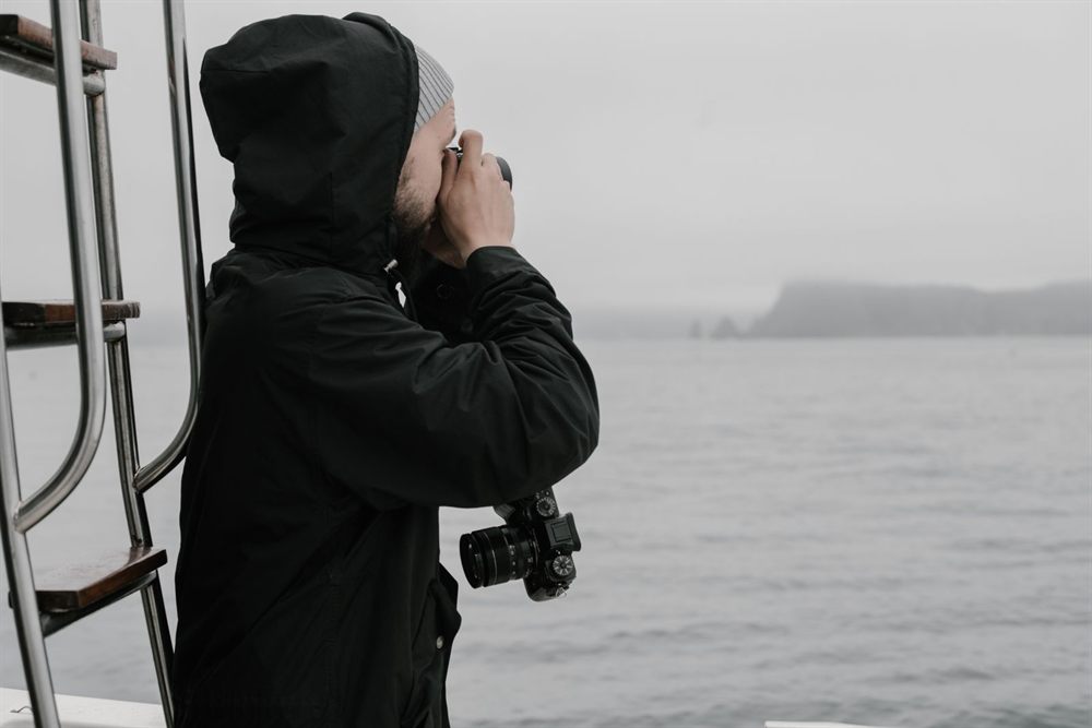 Photographer in a dark jacket shooting a misty coastline from a boat