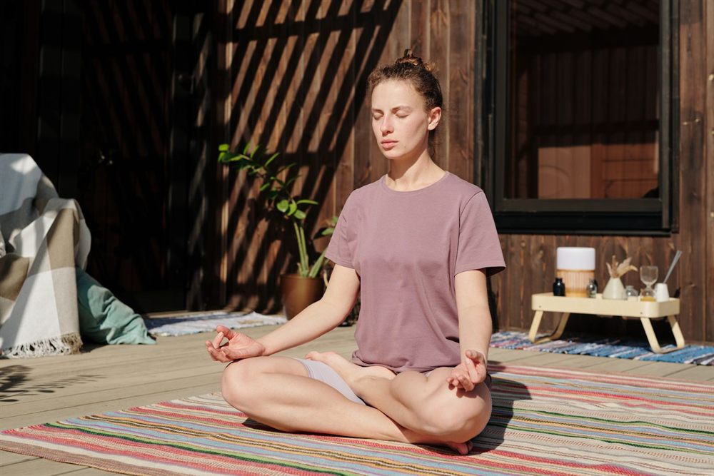 Woman meditating cross-legged on a sunny wooden deck